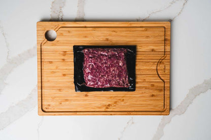 Packaged ground beef on a wooden cutting board with a marble background