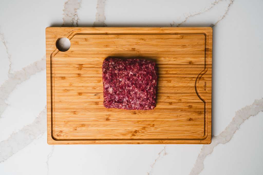 Square of ground beef on a wooden cutting board with a marble background